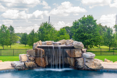 Patterson A - Medford, NJ - A large rock waterfall in the middle of a swimming pool surrounded by lush green grass and trees