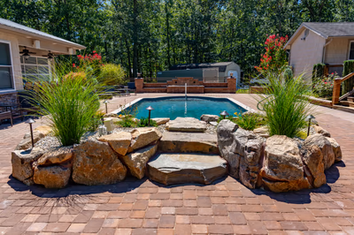 Multi-tiered natural stone boulder waterfall cascading into a pool bordered by lush ornamental grasses