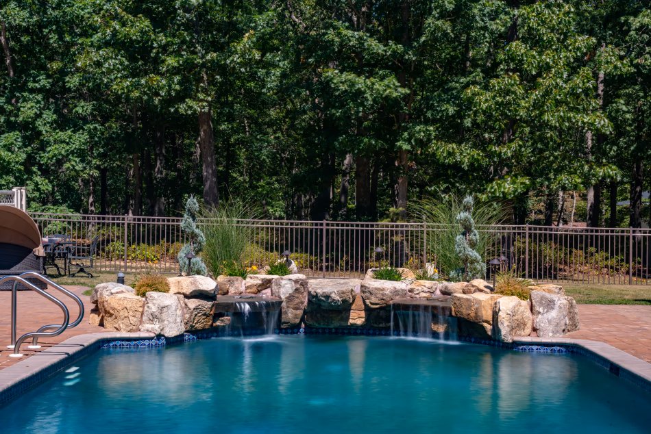 Single-tier natural stone boulder waterfalls cascading into a pool with surrounding trees and plants