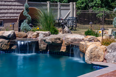 Dual sheet-style natural stone boulder waterfalls flowing into a pool with surrounding ornamental plants