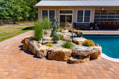Multi-tiered natural stone boulder waterfall cascades into a pool surrounded by lush landscape plants