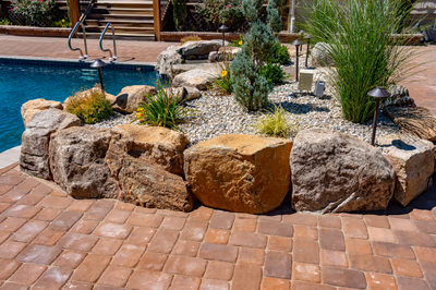 Multi-tiered natural stone boulder waterfalls cascading into a pool with pavers and lush plants