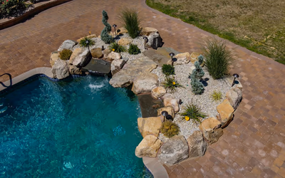 Two-tiered natural stone boulder waterfall cascading into a pool with ornamental rock garden landscaping
