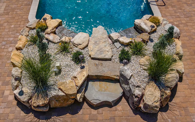 Multi-tiered natural stone waterfall cascading into a pool surrounded by ornamental grasses and gravel
