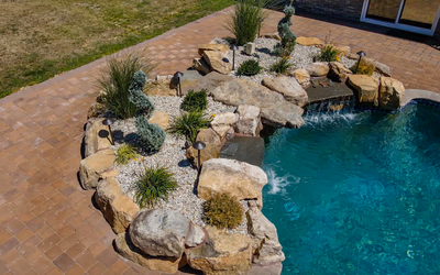 Multi-tiered natural stone boulder waterfall cascading into a pool bordered by ornamental garden plants