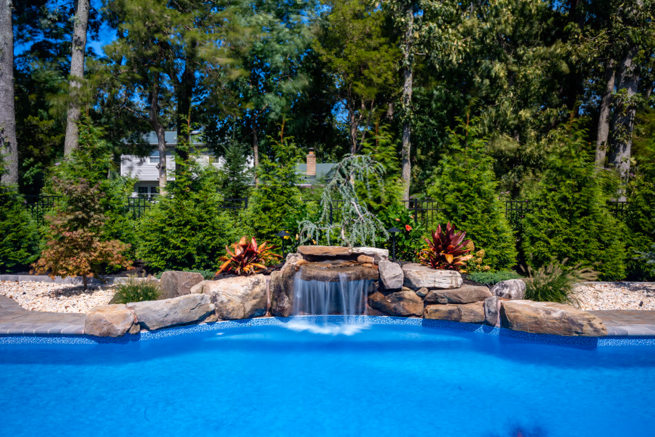 Two-tiered natural stone boulder waterfall cascading into a blue pool surrounded by lush greenery