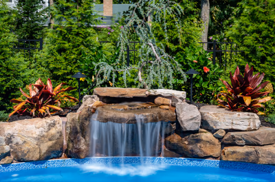 Two-tiered natural stone waterfall cascading into a backyard pool surrounded by lush tropical greenery