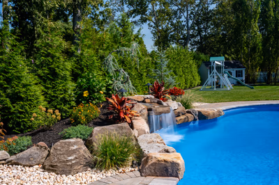 Two-tiered natural stone boulder waterfall cascading into a blue pool with lush tropical plants