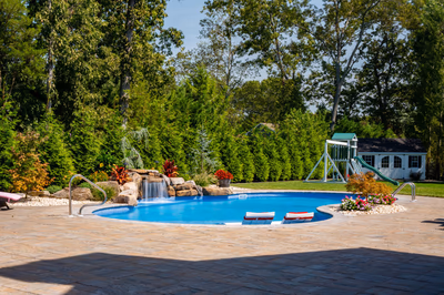 Two-tiered natural stone boulder waterfall cascades into a freeform pool with lush green landscaping