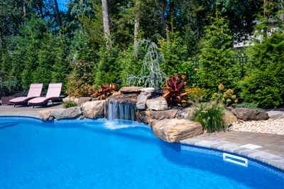 Two-tiered natural stone boulder waterfall cascading into a pool surrounded by lush green plants