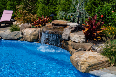 Multi-tiered natural stone boulder waterfall cascading into a swimming pool with lush tropical plants