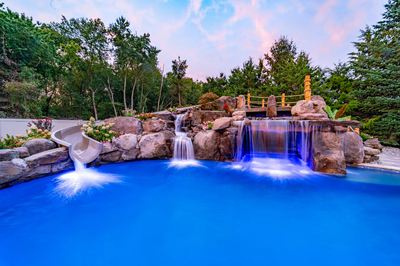 Multi-tiered natural stone boulder waterfalls cascading into a pool with lush trees and flowers