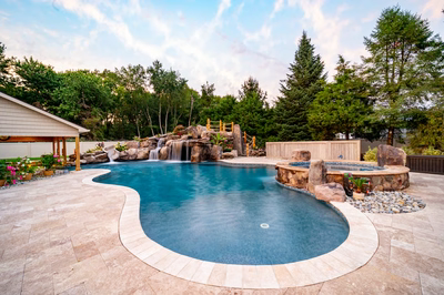 Multi-tiered natural stone boulder waterfall cascading into a freeform pool with lush forest surroundings