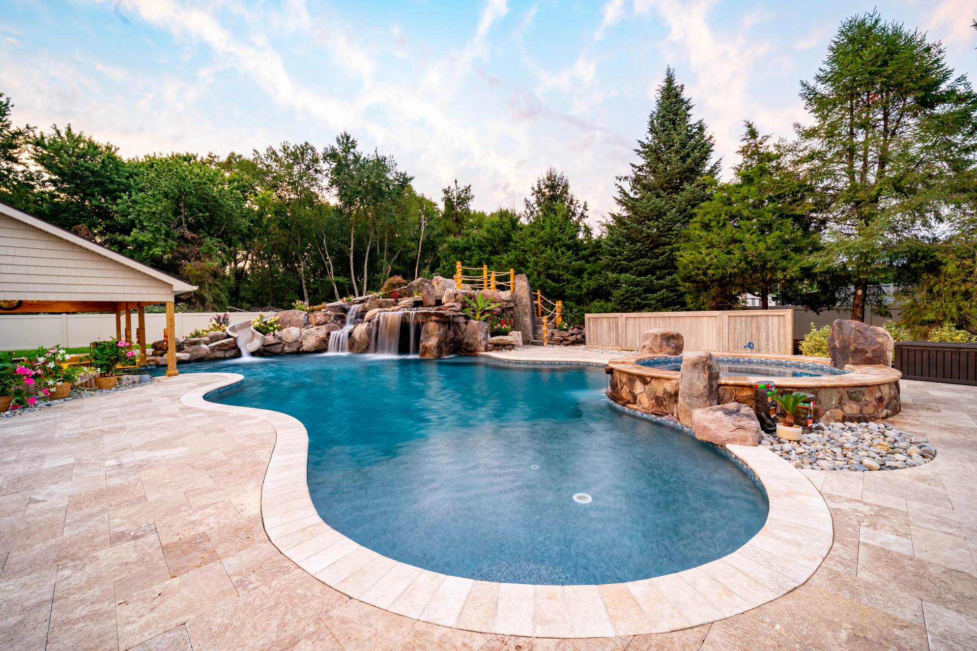 Multi-tiered natural stone boulder waterfall cascading into a freeform pool with lush forest surroundings