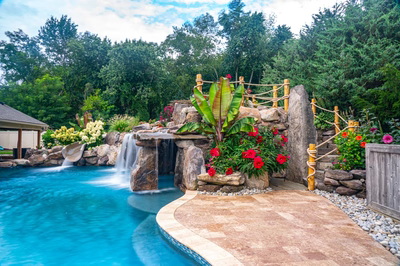 Multi-tiered natural stone boulder waterfalls cascade into a freeform pool with lush tropical landscaping
