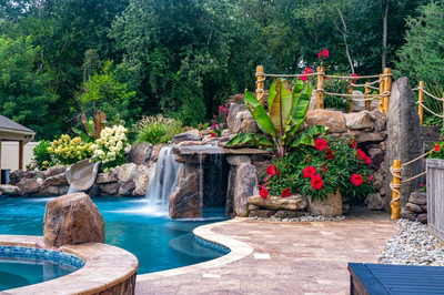 Two-tiered natural stone boulder waterfall cascading into a pool with vibrant tropical landscaping