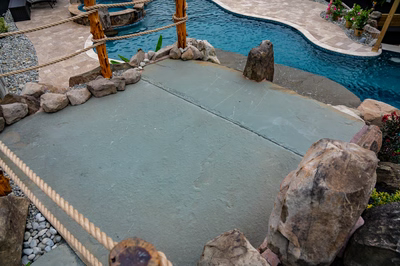 Multi-tiered natural stone boulder waterfall cascading into a freeform pool surrounded by tropical plants