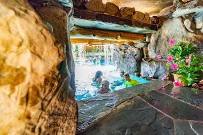 Multi-tiered natural stone boulder waterfall cascading into a pool area with potted pink flowers
