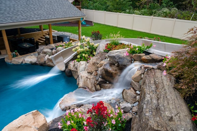 Multi-tiered natural stone boulder waterfalls cascading into a blue pool with lush floral landscaping