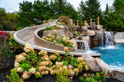 Multi-tiered natural stone waterfalls cascade into a pool surrounded by lush flowering plants