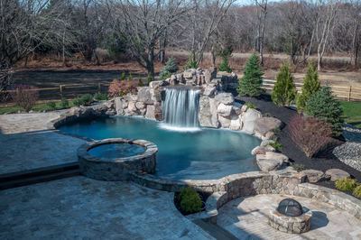 Single-tier natural stone boulder waterfall cascading into a freeform pool with surrounding trees and shrubs