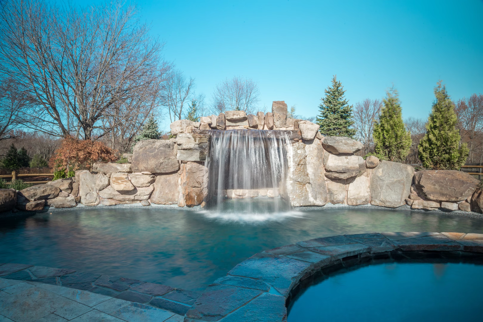 Natural stone boulder waterfall cascading into a pool surrounded by lush evergreen trees