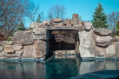 Single-tier natural stone boulder waterfall cascading into a pool with surrounding trees and greenery