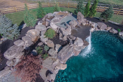 Multi-tiered natural stone boulder waterfall cascading into a pool with lush evergreen landscaping