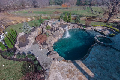 Multi-tiered natural stone boulder waterfall cascading into a freeform pool surrounded by lush evergreens