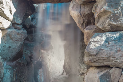Multi-tiered natural stone boulder waterfall featuring curtain flow cascading into a pool with plants