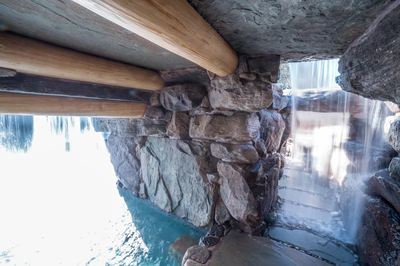 Single-tier sheet flow natural stone boulder waterfall cascading into a pool with lush greenery