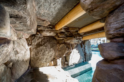 Multi-tiered natural stone boulder waterfall cascading into a clear pool with lush tropical landscaping