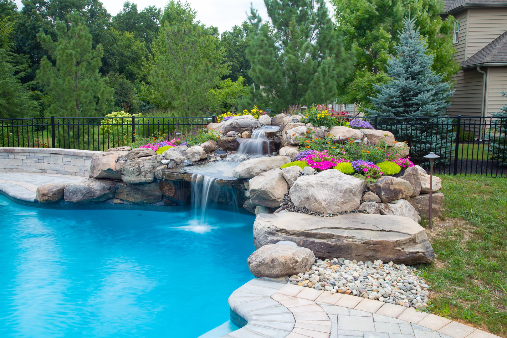 Natural stone boulder waterfall cascading into a pool surrounded by colorful garden plants