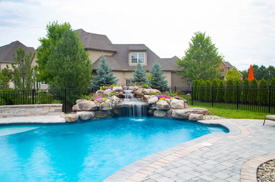 Two-tiered natural stone boulder waterfall cascading into a pool bordered by lush garden plantings
