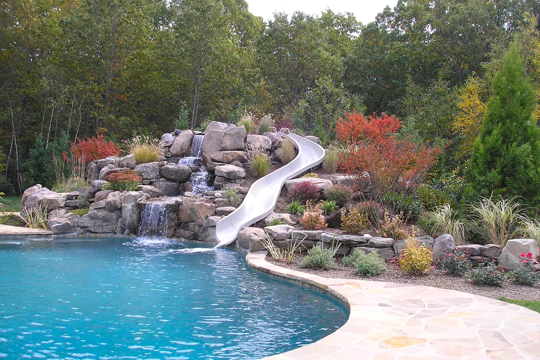 Multi-tiered natural stone boulder waterfall cascading into a pool surrounded by lush, colorful landscaping