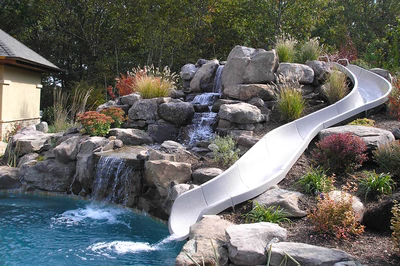 Multi-tiered natural stone boulder waterfall cascading into a pool with lush ornamental garden plants