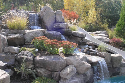 Multi-tiered natural stone boulder waterfall cascading into a pool with lush ornamental garden plants