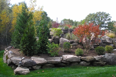 Multi-tiered natural stone boulder waterfall cascading through lush greenery and colorful autumn shrubs