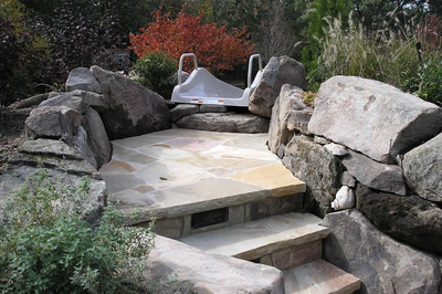 Multi-tiered natural stone boulder waterfall cascading into a pool surrounded by lush garden greenery