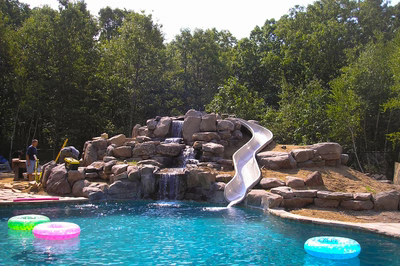 Three-tiered natural stone boulder waterfall cascading into a swimming pool surrounded by lush greenery