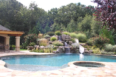 Multi-tiered natural stone boulder waterfall cascading into a freeform pool with lush garden greenery