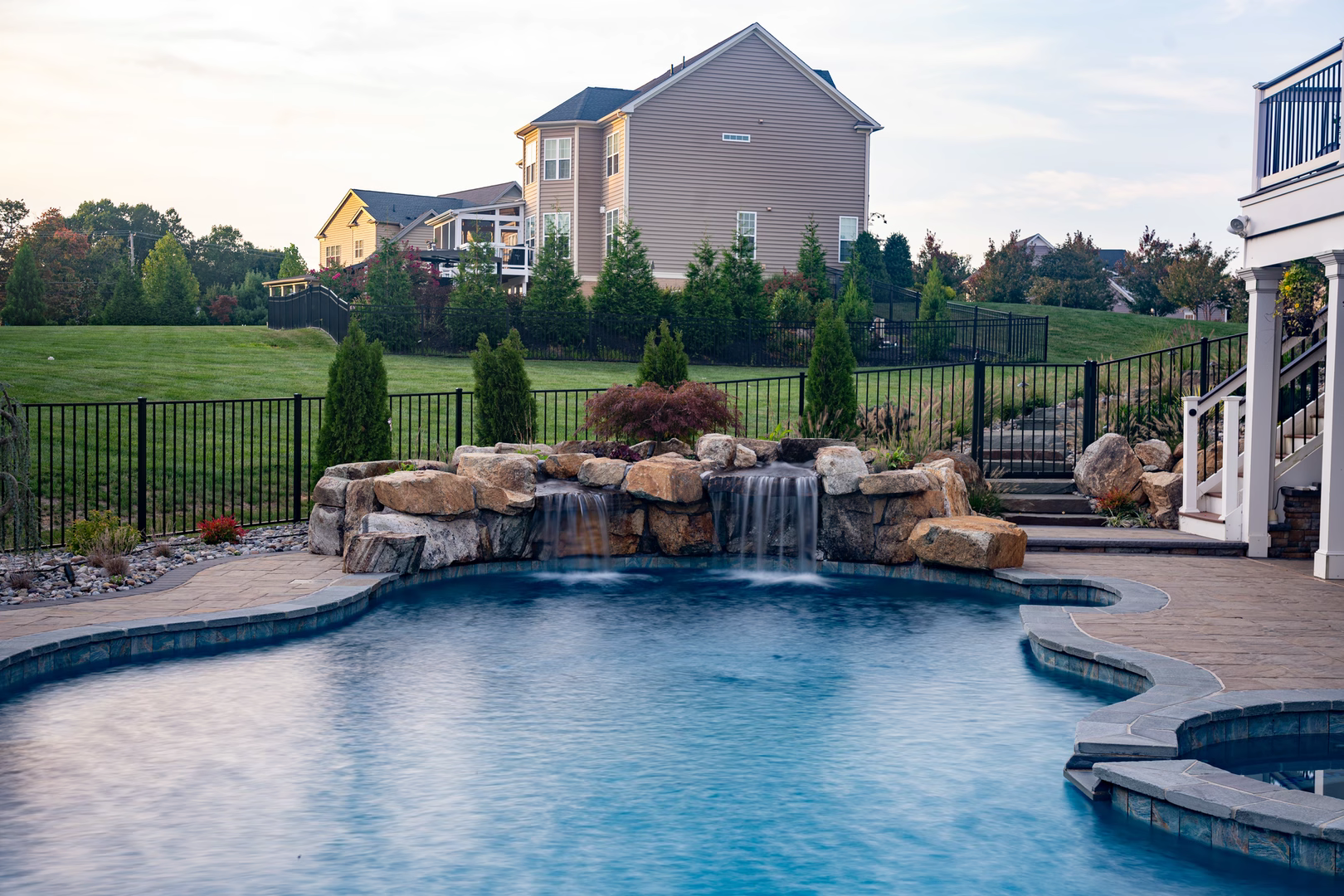 Natural stone boulder waterfall cascading into a backyard pool with lush landscaping