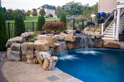 Two-tiered natural stone boulder waterfalls flow into a pool surrounded by lush garden plants