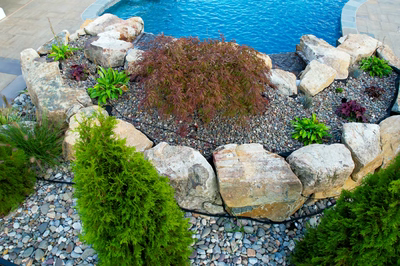 Multi-tiered natural stone boulder waterfall cascading into a pool surrounded by lush, colorful garden plants