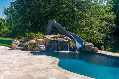 Multi-tiered natural stone boulder waterfall cascading into a pool with slide and lush landscaping