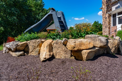 Two-tiered natural stone boulder waterfall cascading into a pool with lush garden plants