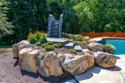 Multi-tiered natural stone boulder waterfall cascading into a freeform pool with lush garden plants