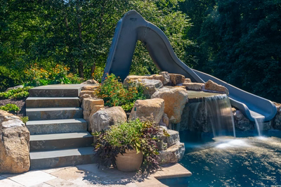 Single-tiered natural stone boulder waterfall cascading into a pool surrounded by lush garden plants