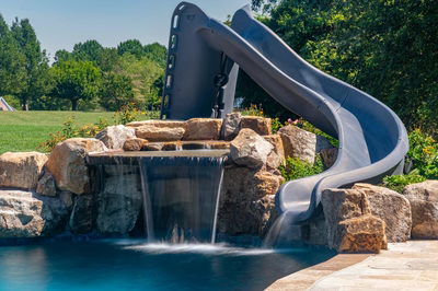 Double-tiered natural stone boulder waterfall cascading into a pool surrounded by lush garden plants