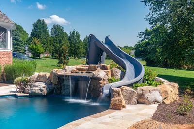 Two-tiered natural stone boulder waterfall cascading into a pool surrounded by lush green landscaping